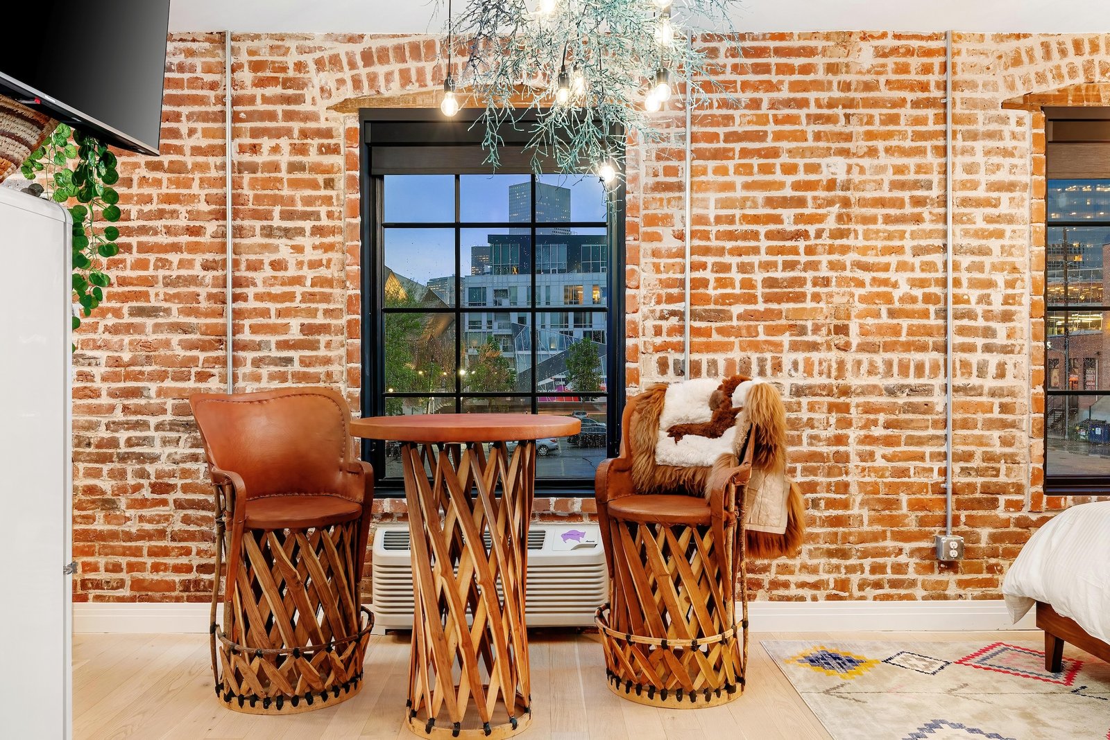 Inviting vacation rental space with exposed brick walls, rustic furniture, and city view through large windows. Click to order a Vacation Rentals Photography Package for standout property listings.